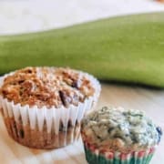 Regular and mini zucchini muffins on a wooden table with a zucchini behind them