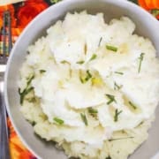 Mashed Potatoes with chives in a gray bowl with a fork on top of a harvest napkin