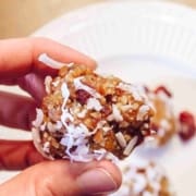 Hand holding apricot almond butter energy ball over white plate with several energy balls