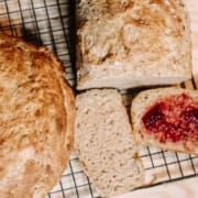 two loaves of bread on a cooling rack with 2 slices of bread, one with jam spread on the surface